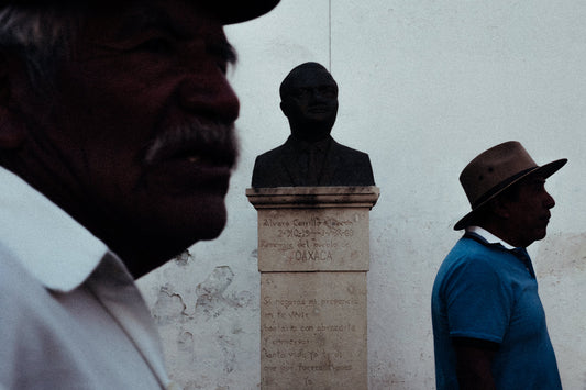 Photographic Art by Nick Sparks of two men walking past a statue of a historic figure in Oaxaca. 